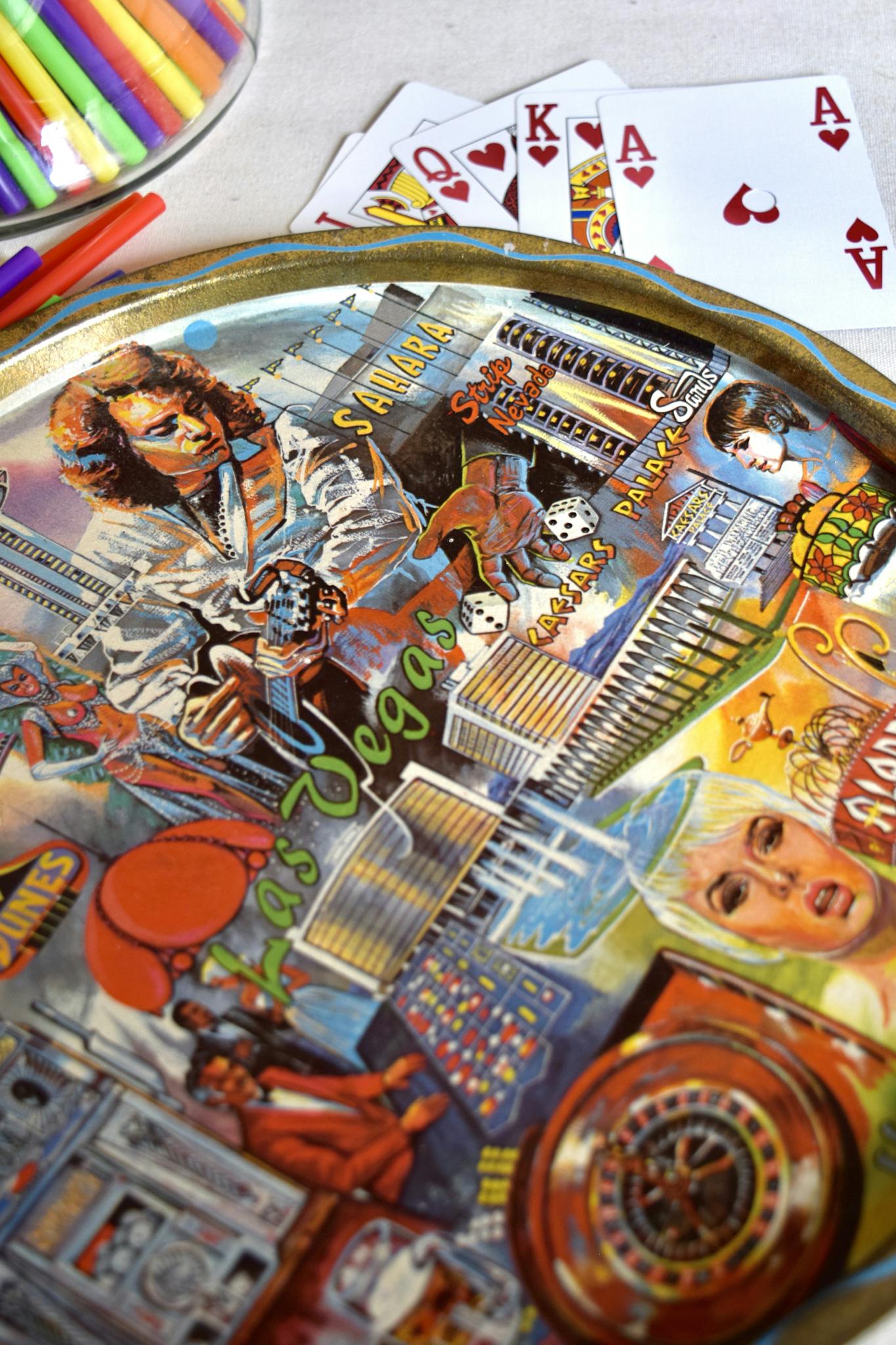 Top view of round metal tray representing colorful gambling and people near various cards with kit of stationery on table at home